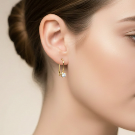 Close-up of a woman wearing a gold earring with a clear gemstone on a neutral background