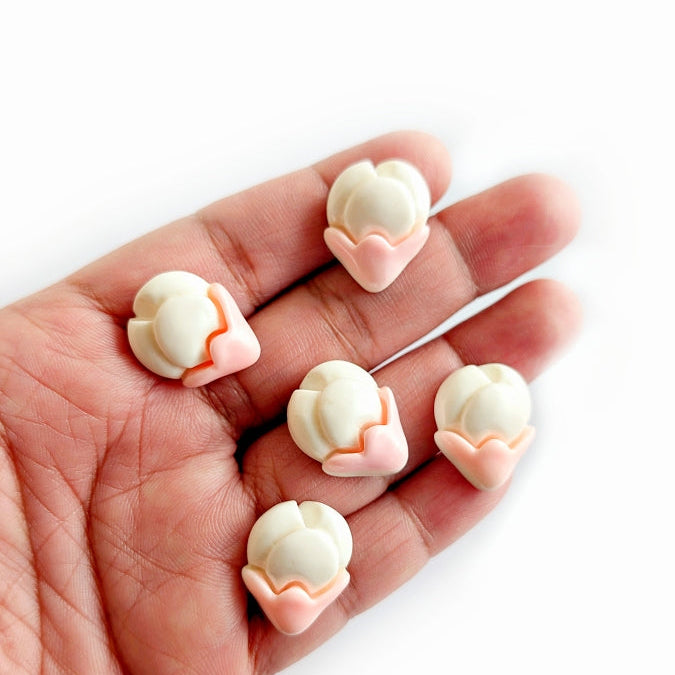 Hand holding small white and pink decorative items on a white background