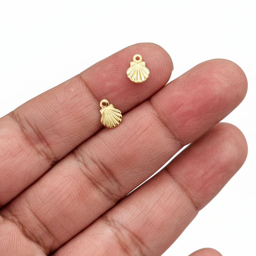 Gold shell charm pendant held in a hand against a black background