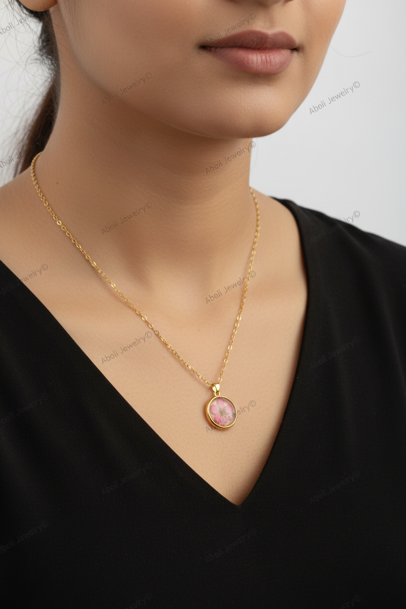 Gold necklace with a pink pendant worn by a model against a neutral background