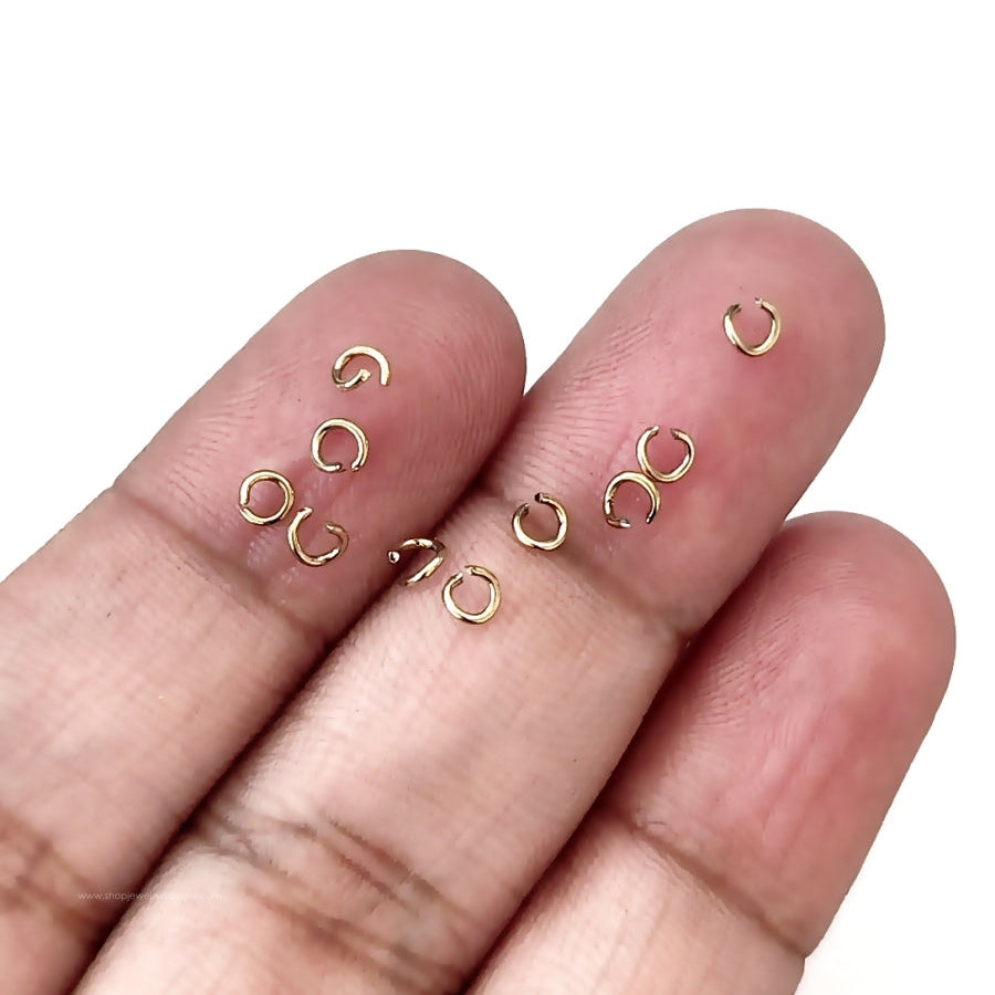 Small gold jewelry components on a person's fingers against a white background