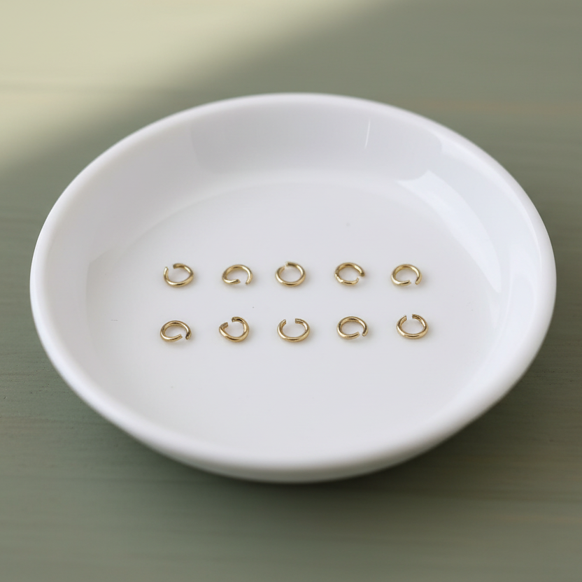 Gold jump rings on a white ceramic dish against a beige background