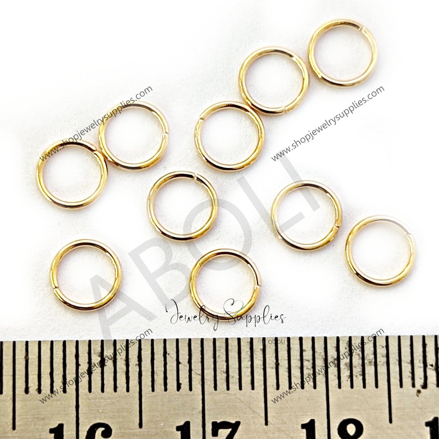 Gold jump rings on a white background with a ruler for scale.