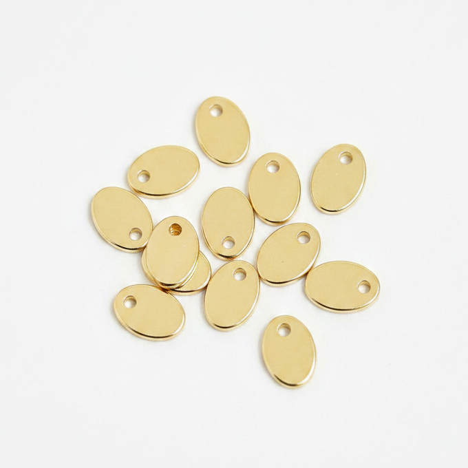 A pile of small oval gold metal charms with pre-drilled holes, arranged on a clean white background.