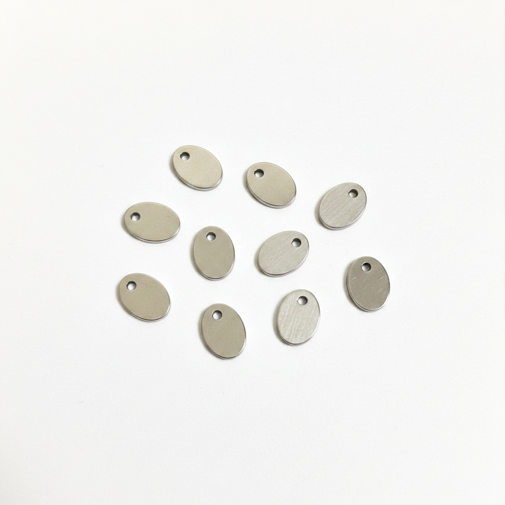 A small oval metal jewelry finding or pendant with a hole, shown above a metal ruler for scale on a white background.
