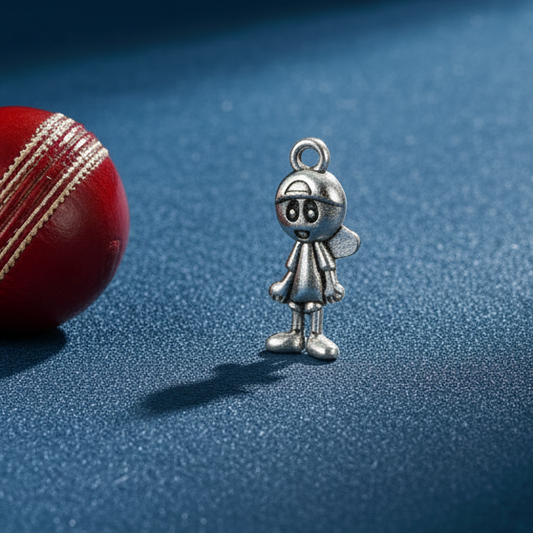 Silver charm resembling a kid next to a red cricket ball on a blue surface