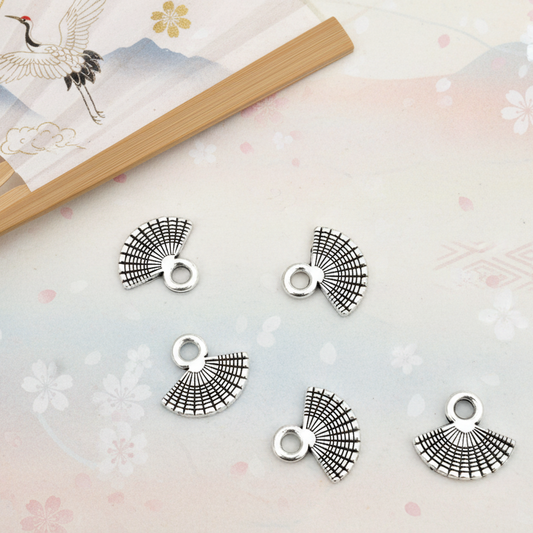 Silver fan-shaped charms on a decorative surface with a fan and floral patterns.