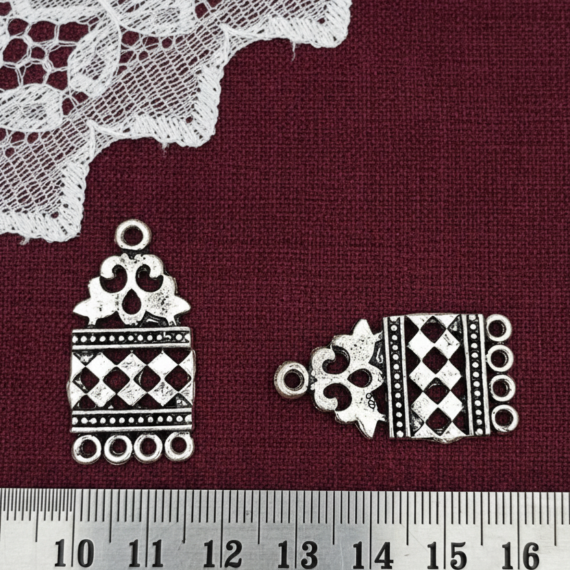 Decorative metal charms on a red fabric background with a ruler for scale.