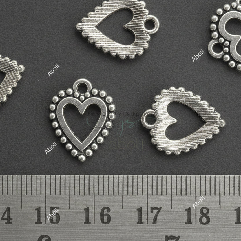 Heart-shaped metal pendants on a dark surface with a ruler for scale.