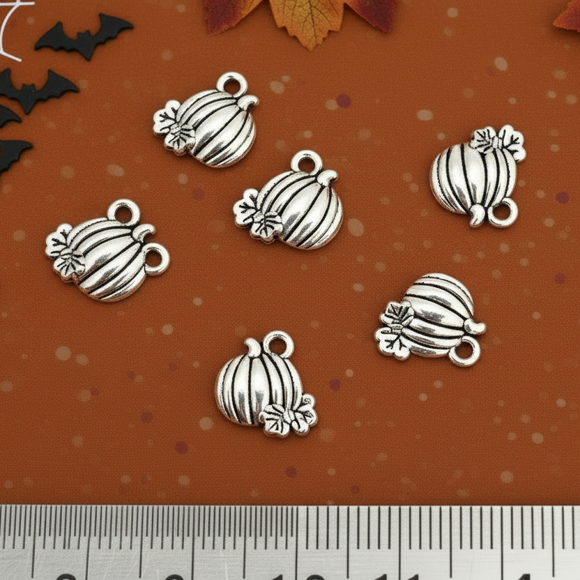 Silver pumpkin-shaped charms on a brown surface with leaves and bats.