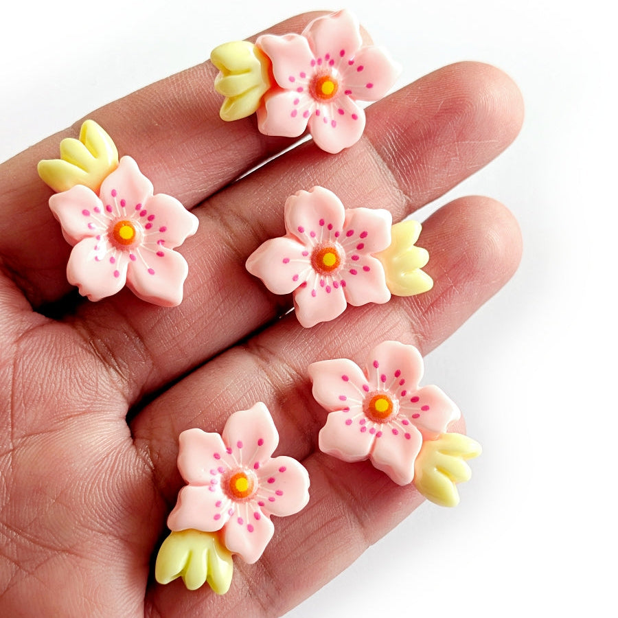 Pink flower-shaped cabochons held in a hand against a white background