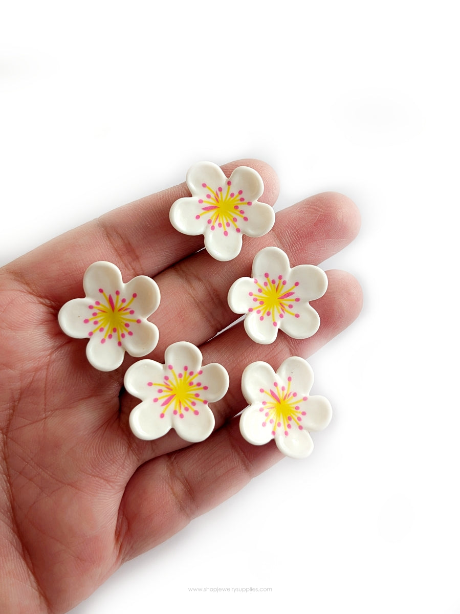 Hand holding five white flower-shaped cabochons with yellow centers on a white background