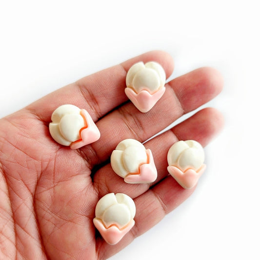 Hand holding small white and pink decorative items on a white background