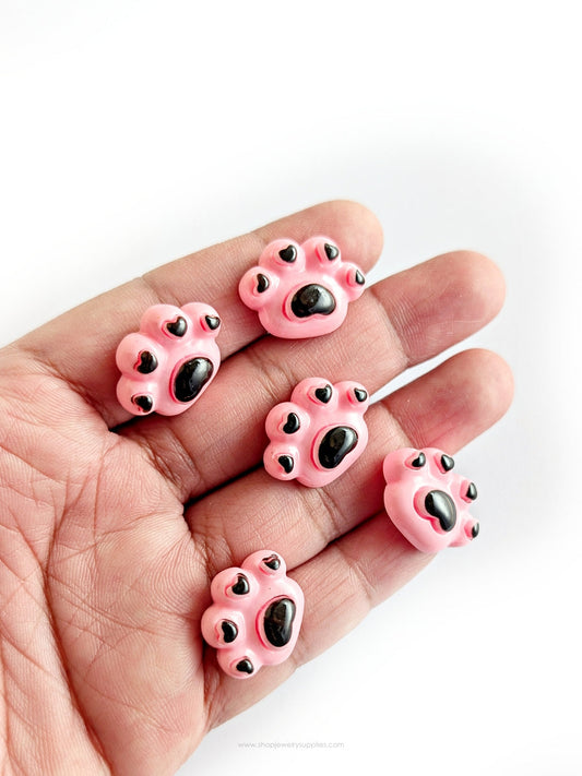 Pink paw-shaped cabochon held in a hand on a white background