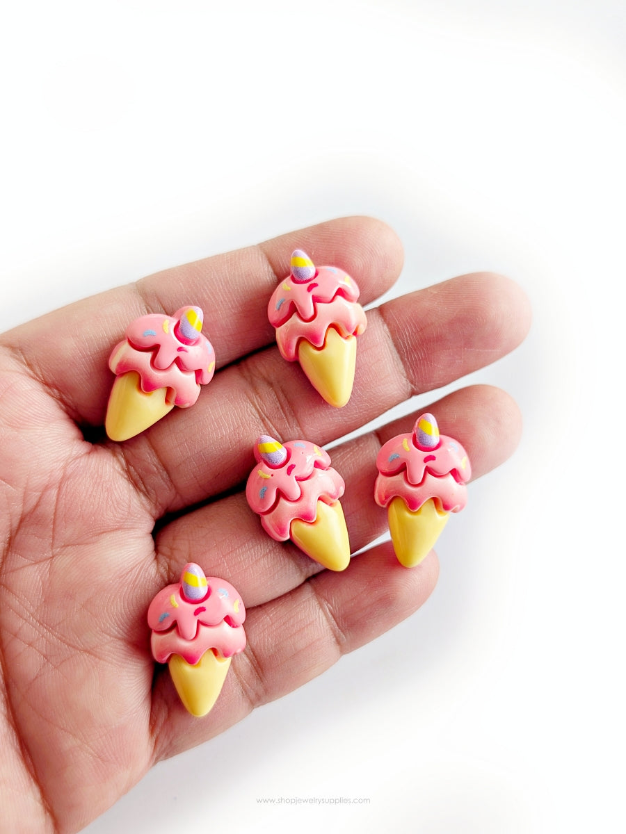 Ice cream cone-shaped cabochons with pink tops and yellow bases held in a hand on a white background