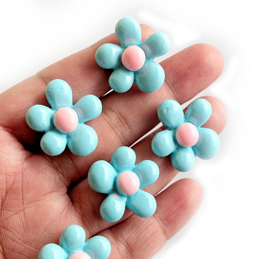 Blue flower-shaped cabochons with pink centers held in a hand against a white background