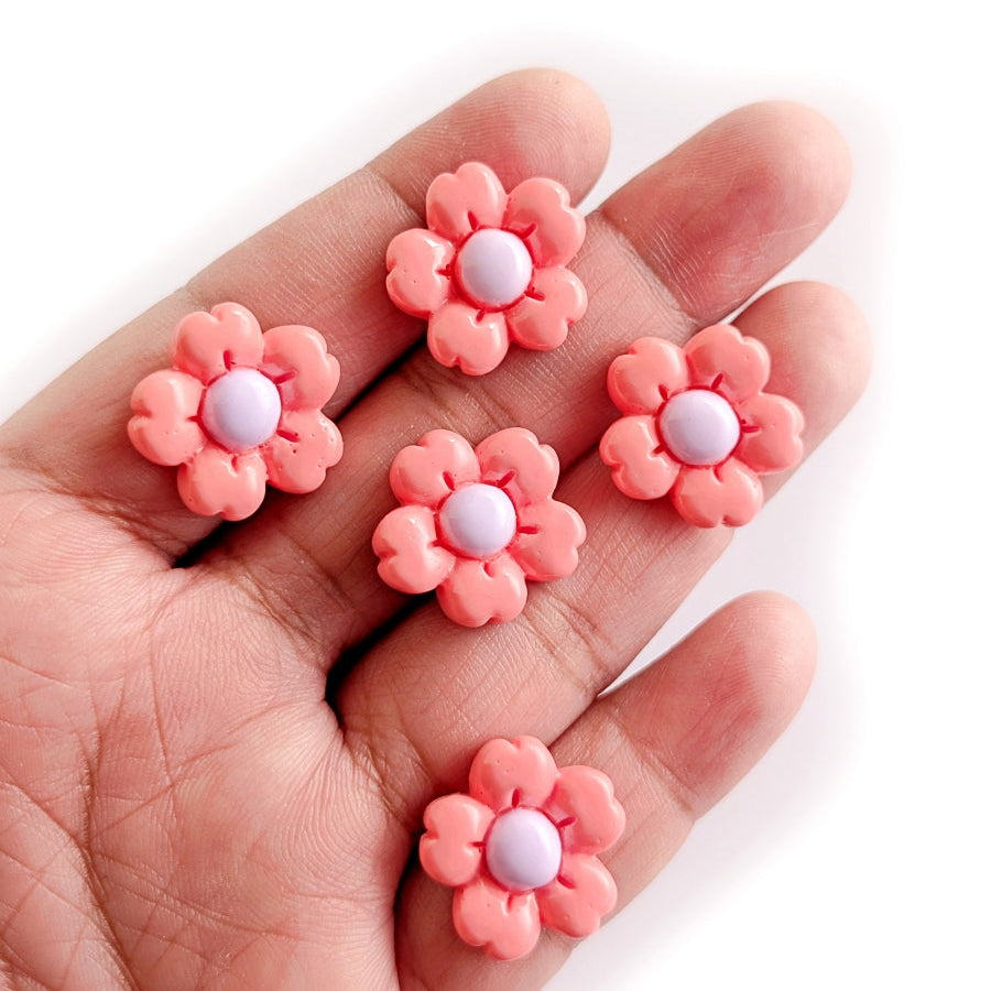 Pink flower-shaped cabochons with white centers held in a hand against a white background