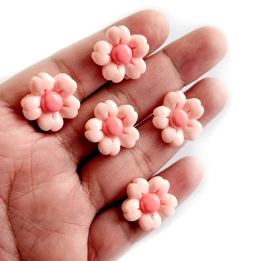 Pink flower-shaped cabochons on a hand against a white background