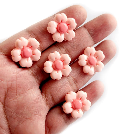 Pink flower-shaped cabochons on a hand against a white background