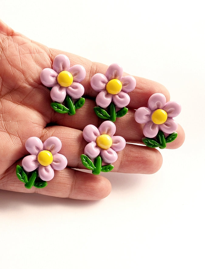 Hand holding small purple flowers with yellow centers and green leaves on a white background