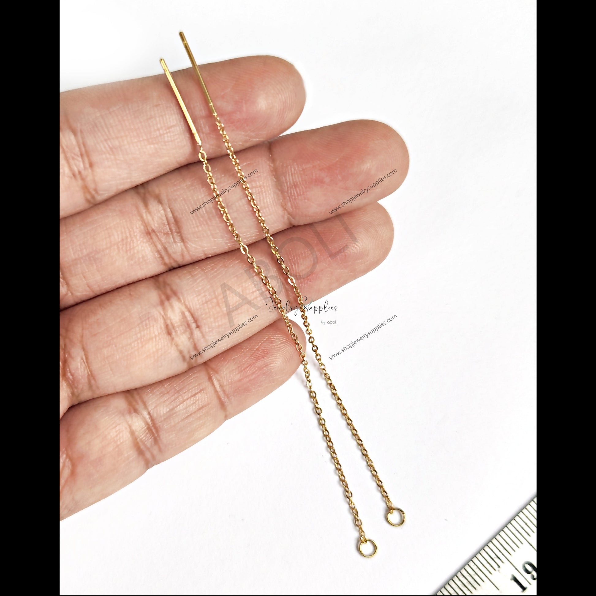 Gold chain held between fingers with a ruler for scale on a white background