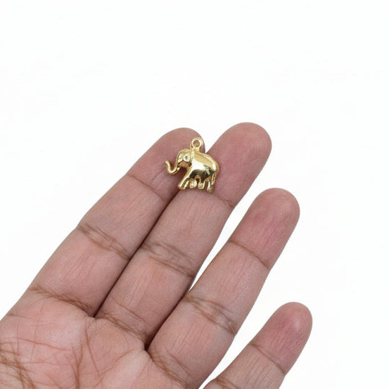 Gold elephant pendant held in a hand with a jewelry-making setup in the background.