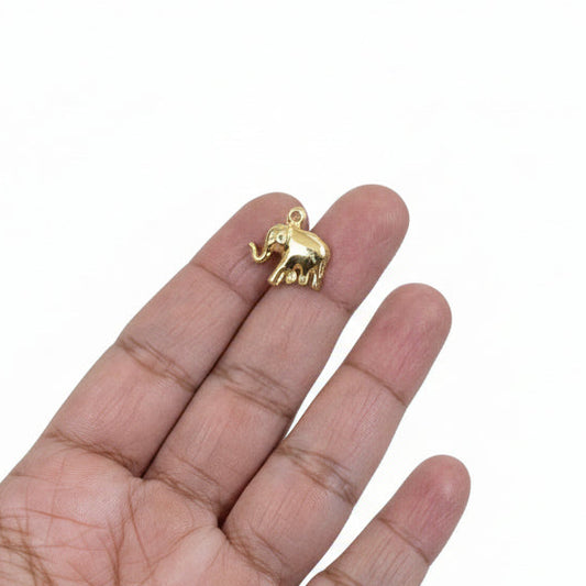 Gold elephant pendant held in a hand with a jewelry-making setup in the background.