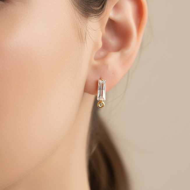 Close-up of a person wearing a gold and clear earring against a neutral background