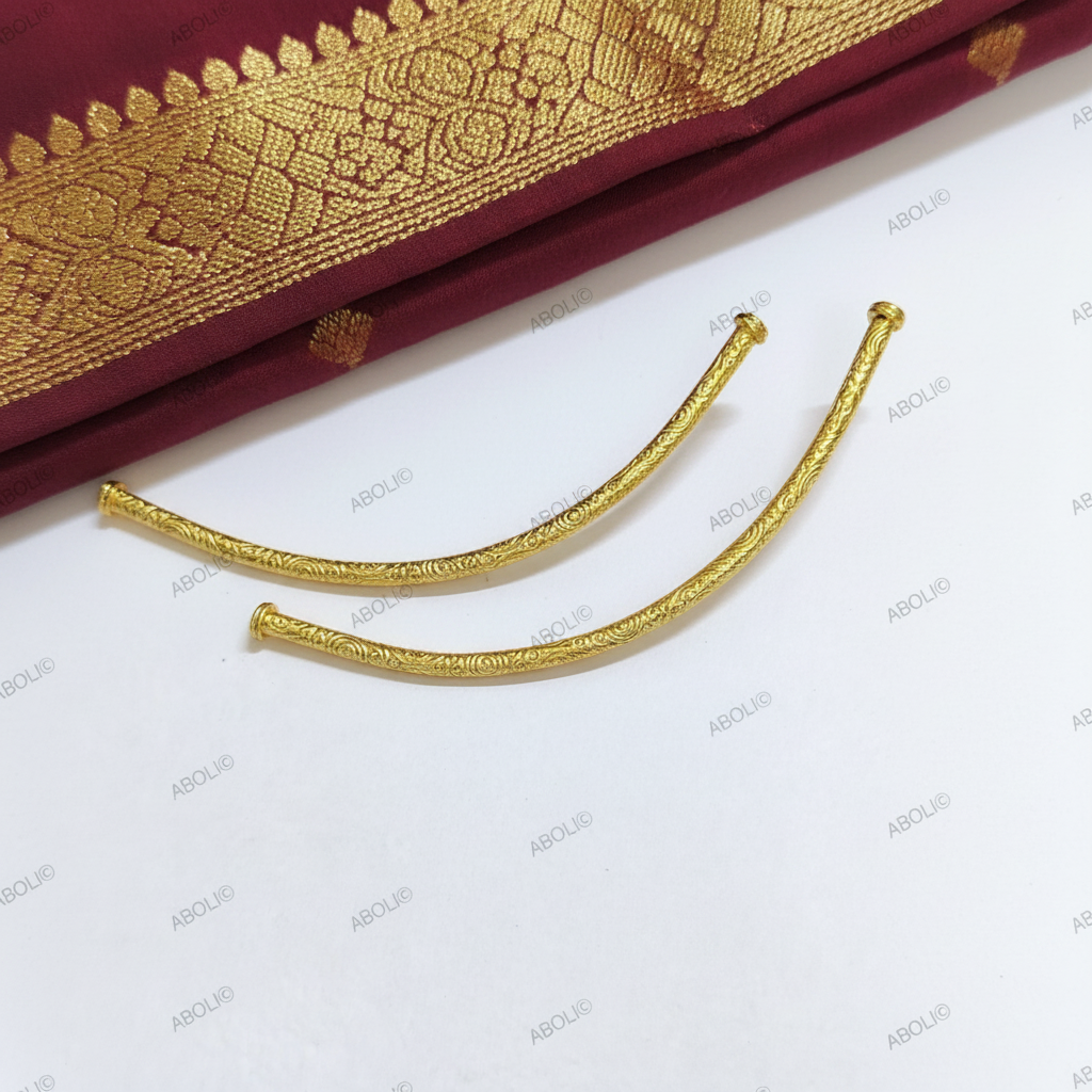 Two gold beads on a white background with a maroon fabric with gold patterns partially visible.