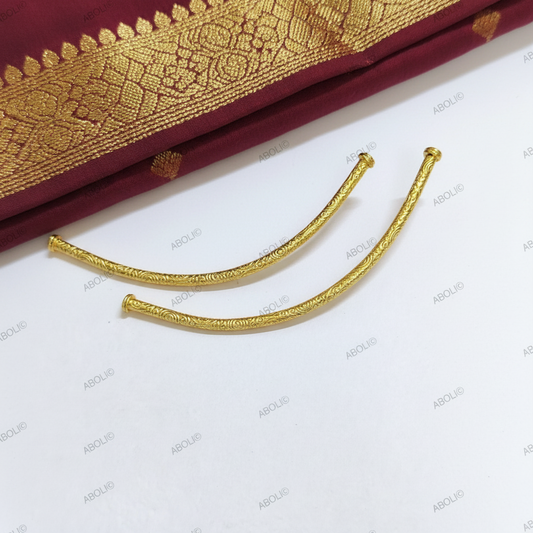 Two gold beads on a white background with a maroon fabric with gold patterns partially visible.