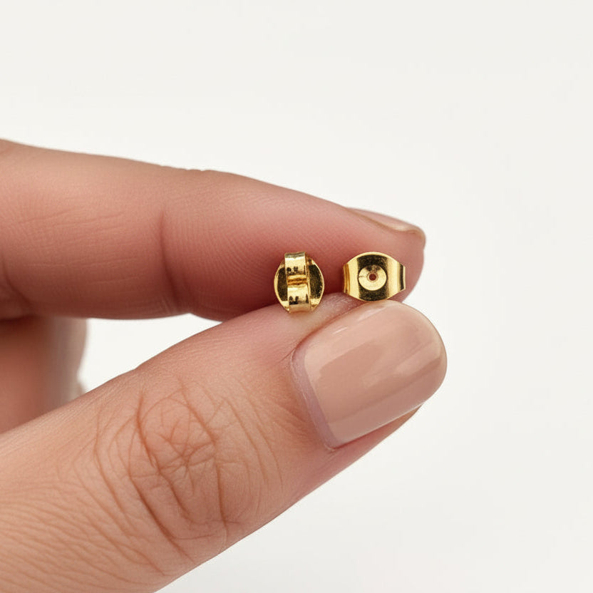 Gold earrings being held between fingers on a white background