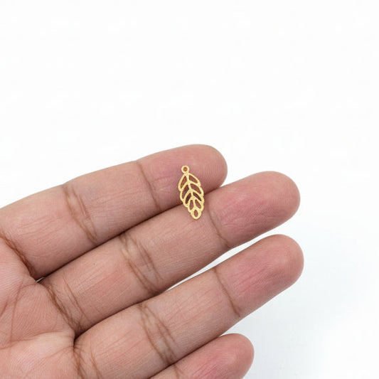 Gold leaf-shaped charm between fingers with jewelry-making materials in the background