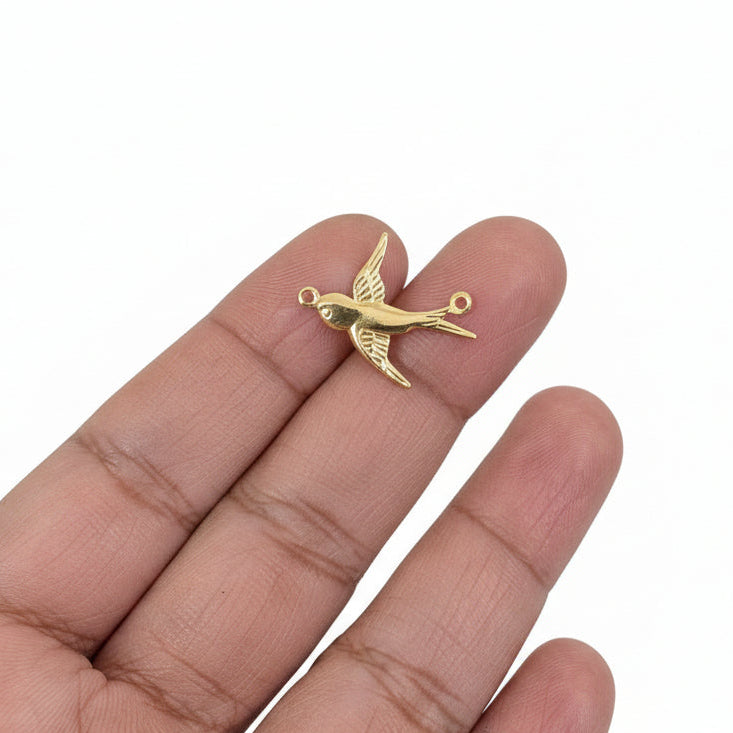 Gold sparrow  held in a hand with a blurred background of jewelry and supplies.