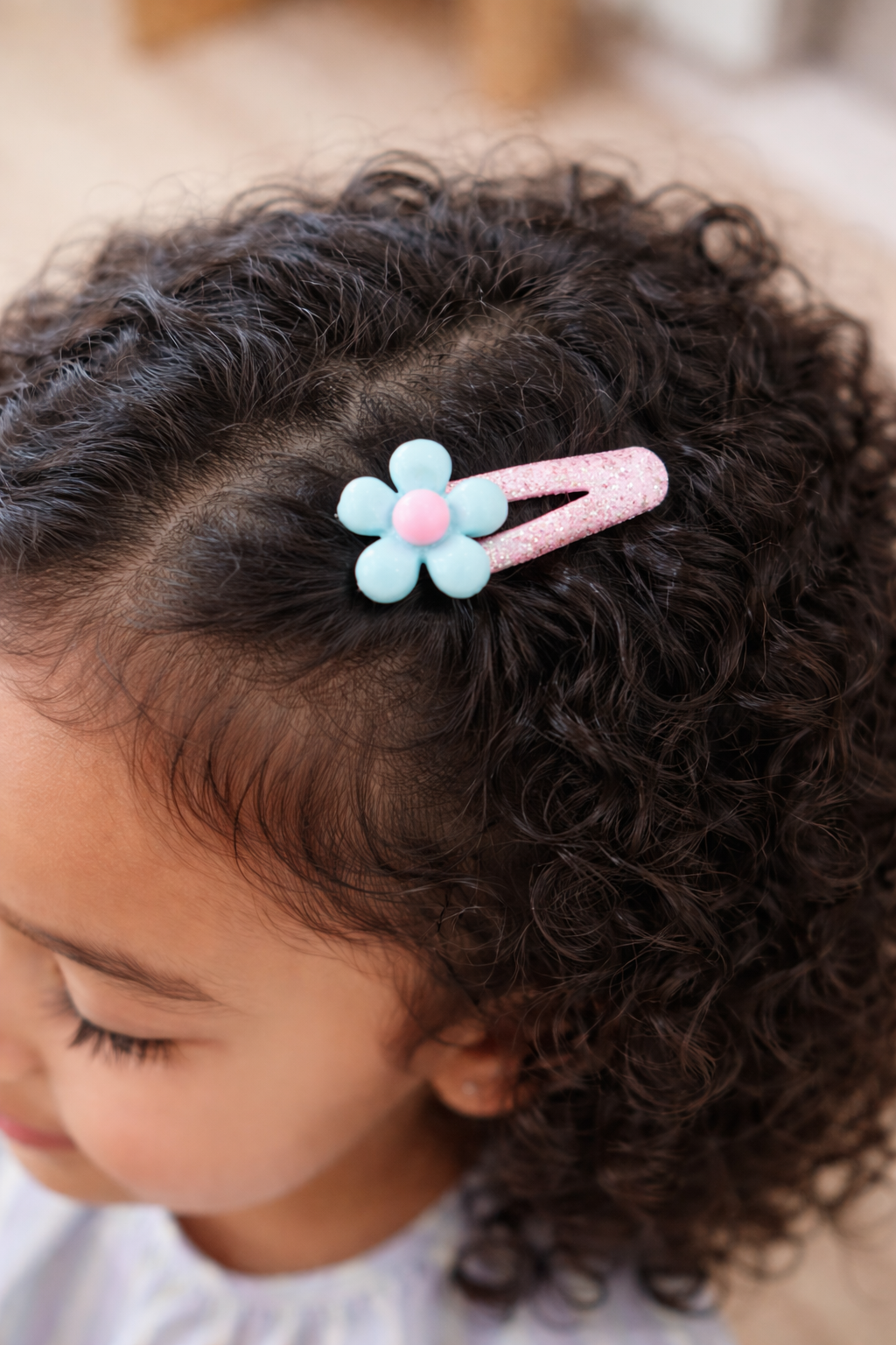Child with curly hair wearing a decorative hair clip with a flower design.