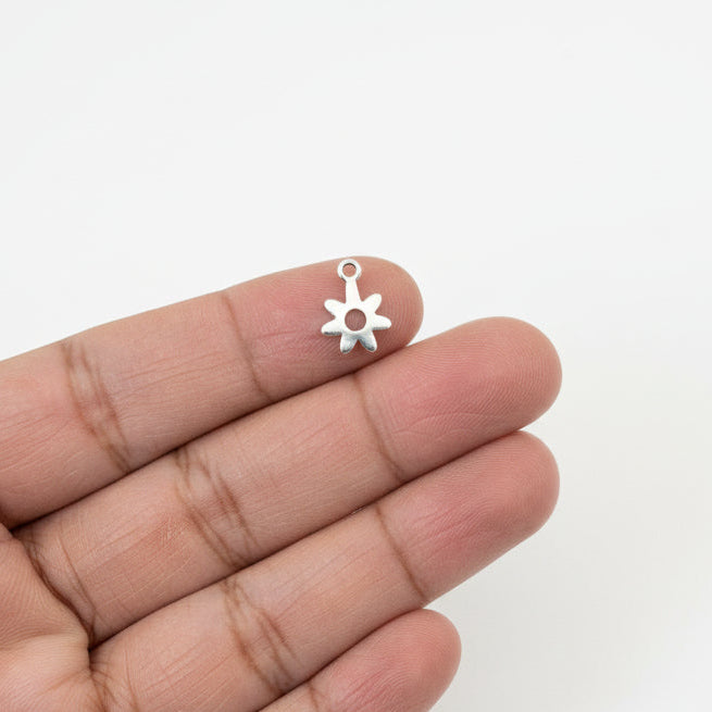 Hand holding a steel flower charm with packaging of similar charms in the background.