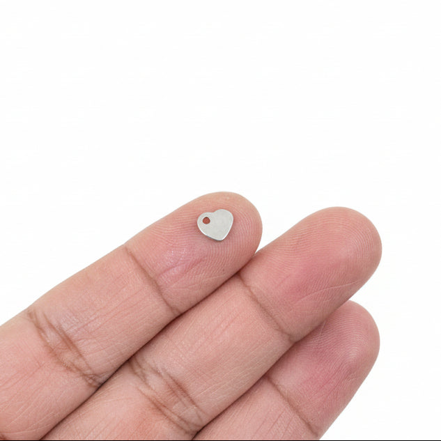 Hand holding a small heart charm object with jewelry components in the background