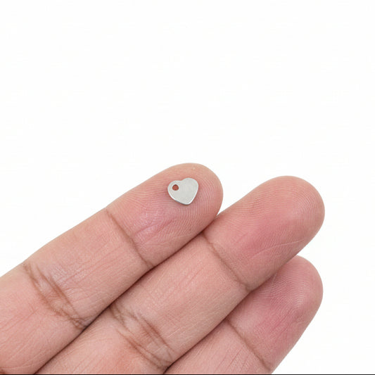 Hand holding a small heart charm object with jewelry components in the background